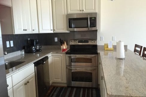 Modern kitchen with white cabinets, black backsplash, and stainless steel appliances, including a microwave and oven. Granite countertop with a roll of paper towels and a kitchen island.