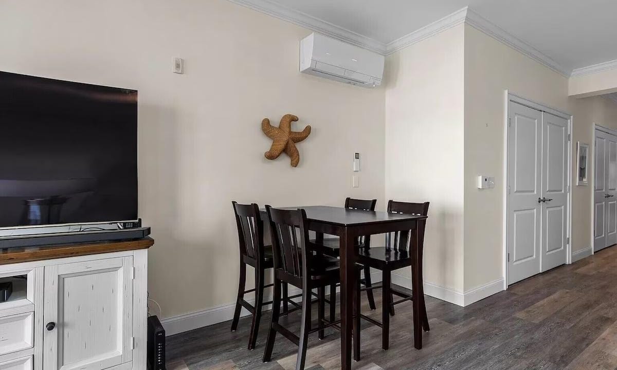 Dining area with a tall table and four chairs, a mounted air conditioning unit, and a starfish decoration on the wall. A TV and cabinet are visible to the left.