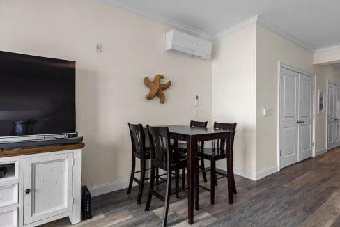 Dining area with a tall table and four chairs, a mounted air conditioning unit, and a starfish decoration on the wall. A TV and cabinet are visible to the left.