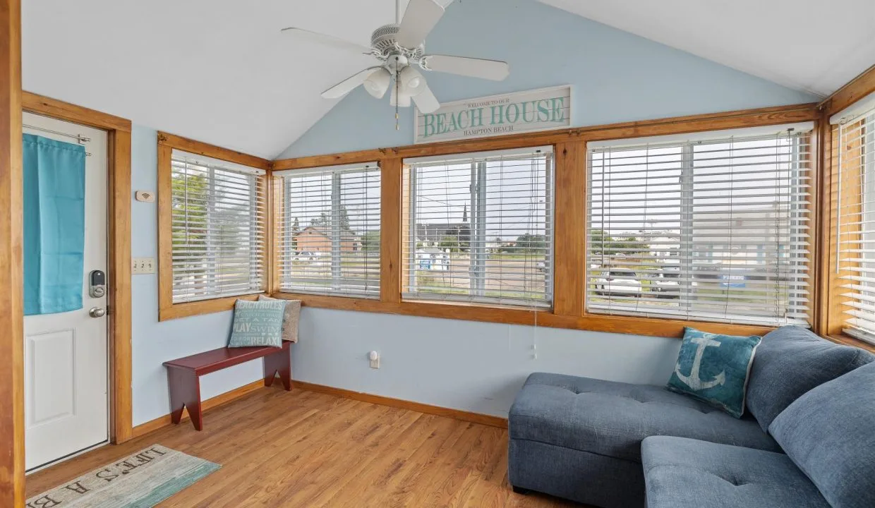 Sunroom with light blue walls, wooden trim, large windows, ceiling fan, blue sectional sofa, bench, and a 