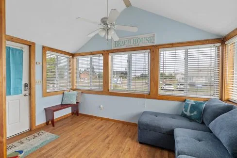 Sunroom with light blue walls, wooden trim, large windows, ceiling fan, blue sectional sofa, bench, and a 