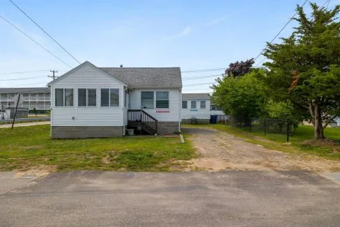 Small white house with a front porch and driveway, surrounded by grass. There's a tree on the right and power lines overhead.