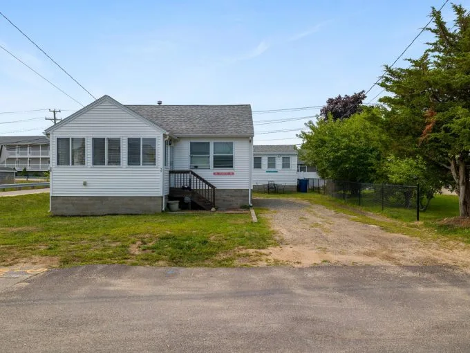 Small white house with a front porch and driveway, surrounded by grass. There's a tree on the right and power lines overhead.