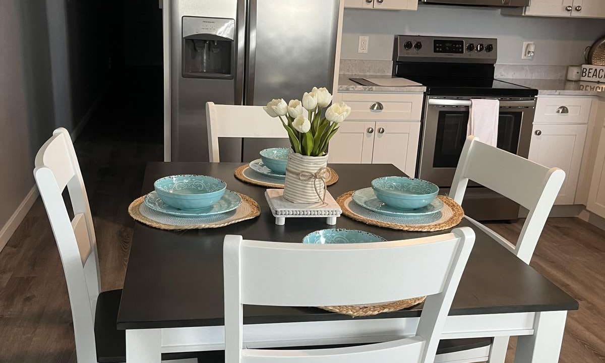 A kitchen with white cabinets, stainless steel appliances, and a small table set for four with blue dishes and a vase of white tulips.