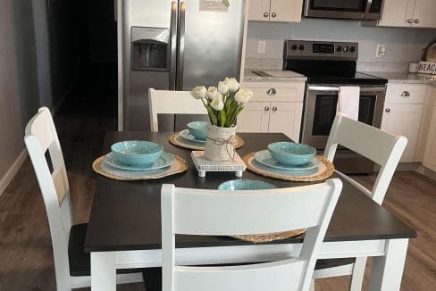 A kitchen with white cabinets, stainless steel appliances, and a small table set for four with blue dishes and a vase of white tulips.