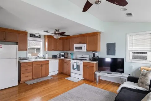 Kitchen and living area with wooden cabinets, white appliances, and a wall-mounted TV. Ceiling fans and light blue walls complete the room.